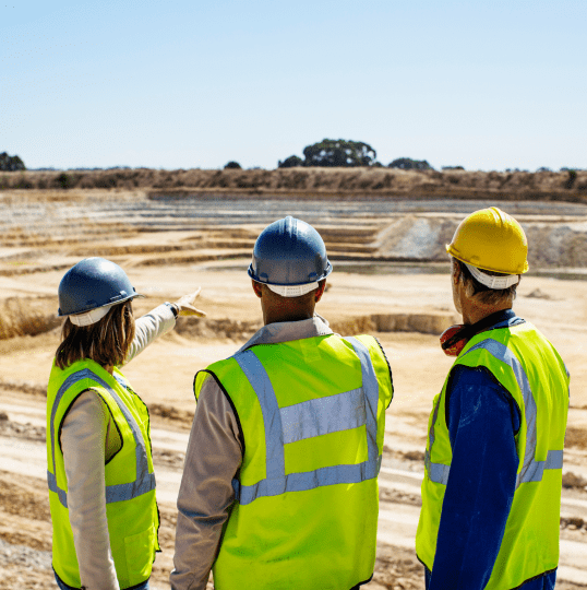 Three workers in safety gear looking out over a project site