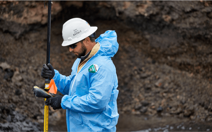 A worker dressed in a blue protective suit and hardhat holding site equipment