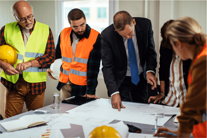 Meeting 1 A team of workers in safety gear and business professionals discussing plans in an office