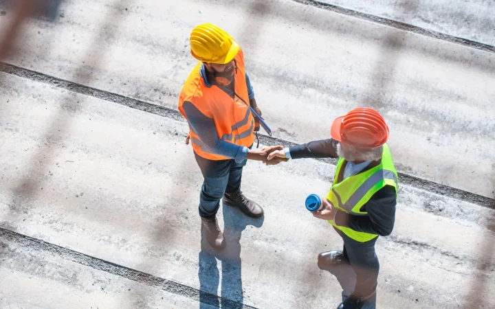 Overhead view of two workers in safety gear shaking hands