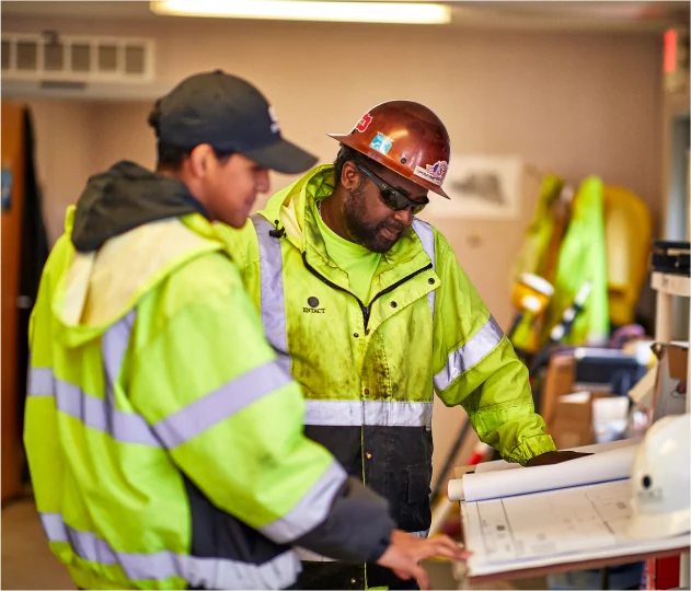 Two workers wearing safety gear looking at a project plan