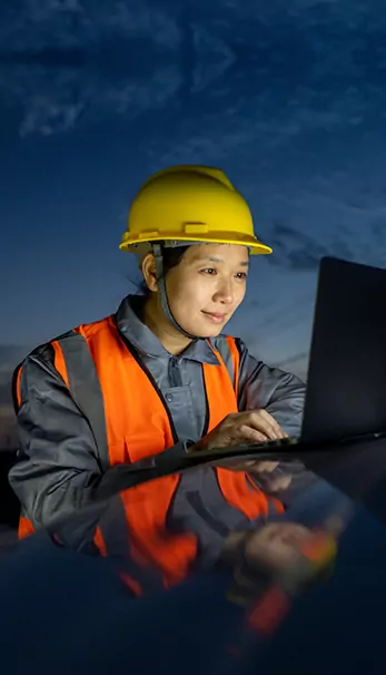 A worker at a project site wearing safety gear and looking at computer