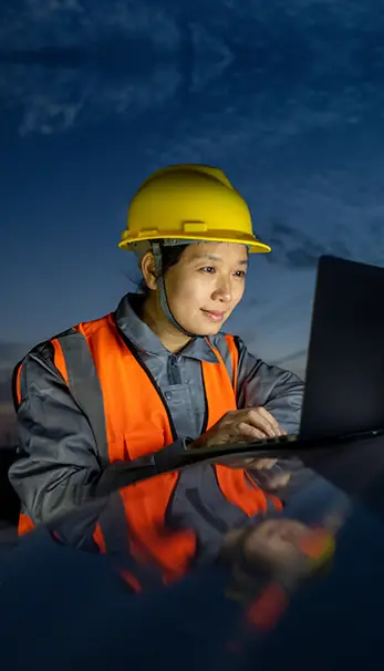 A worker at a project site wearing safety gear and looking at computer