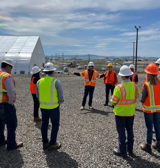 A team of workers in safety gear listening to their manager lead a project site meeting