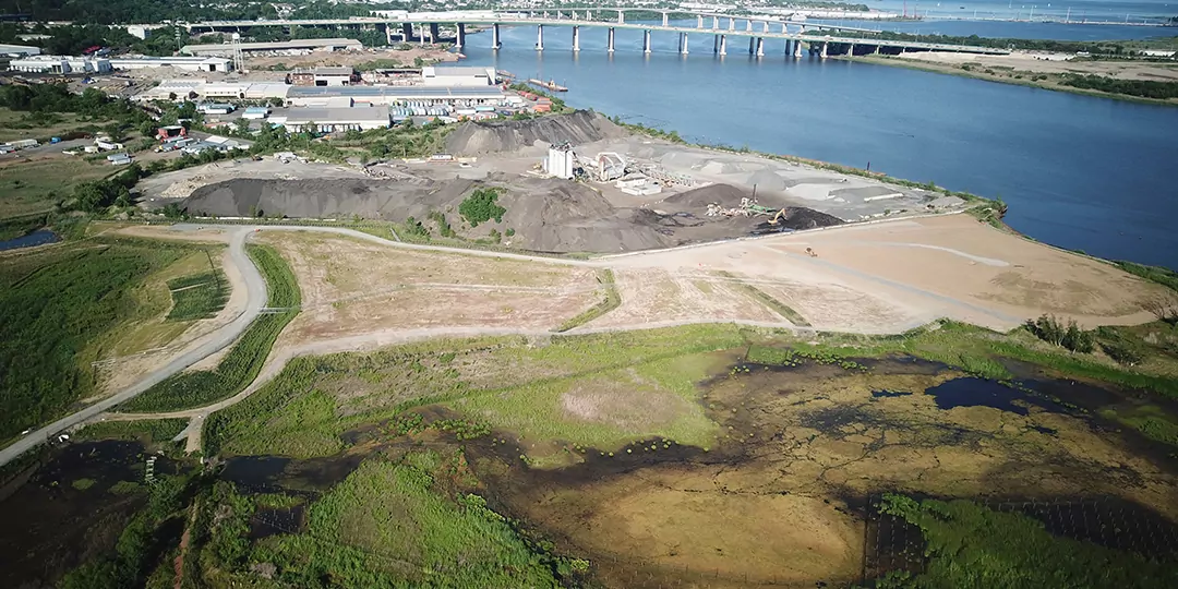 Aerial view of an active project site with water, bridges and buildings in the background