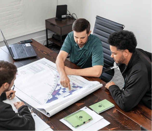 Jersey City Meeting_1.jpg Three individuals in an office looking at project plans on a large wooden desk