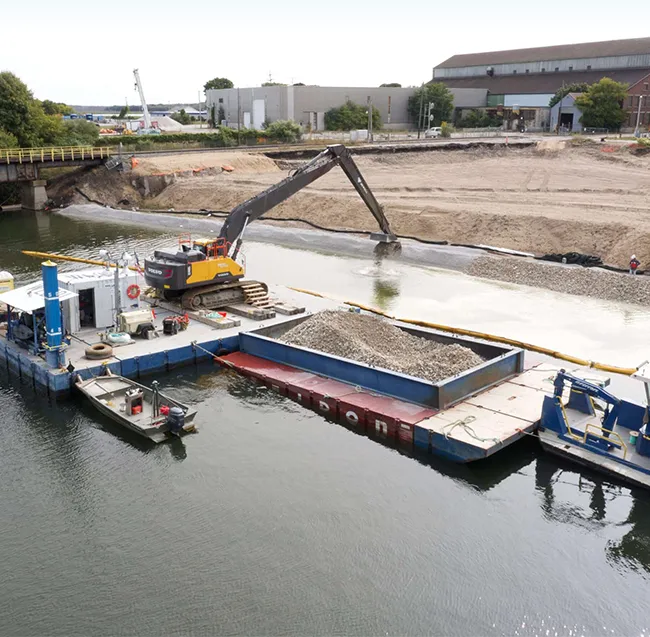 Capping-3-650-e1790273721138 Backhoe and barge at a bank stabilization project site.
