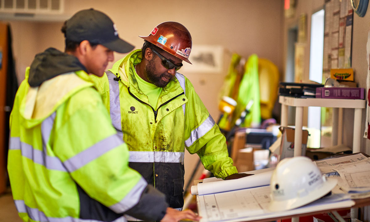 entact workers in yellow neon jackets look over a blueprint