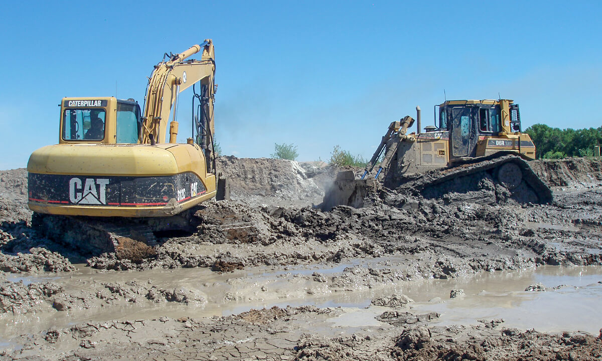 tow excavators digging into the mud at a job site