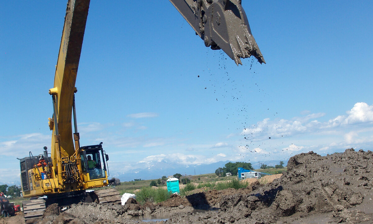 an excavator claw rising from the ground with a load of mud
